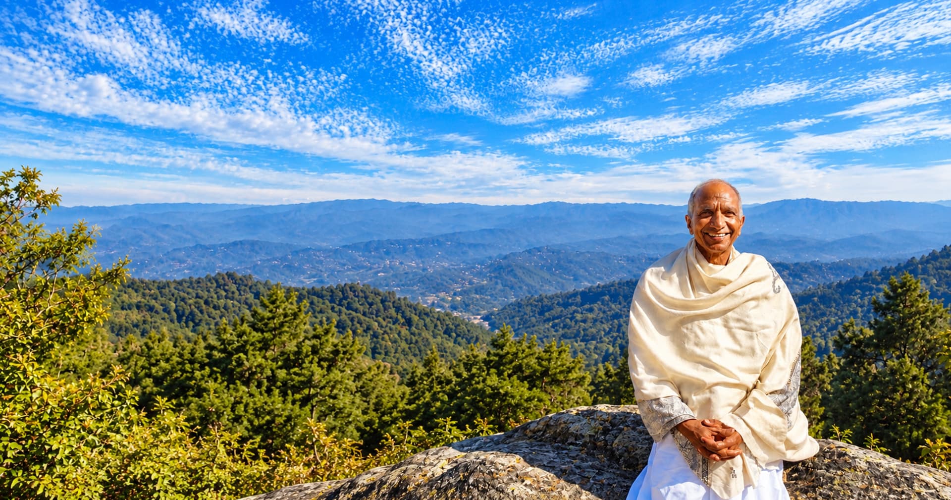 Amar Singh Chandel in a cream shawl, seated on a Himalayan ridge under a wide blue sky